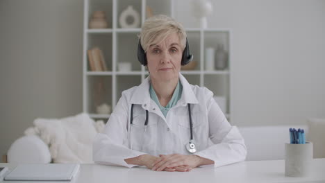 Una-Doctora-Jubilada-Está-Consultando-En-Línea-Mirando-La-Cámara-Y-Asintiendo-Escuchando-Con-Auriculares-El-Servicio-De-Telemedicina